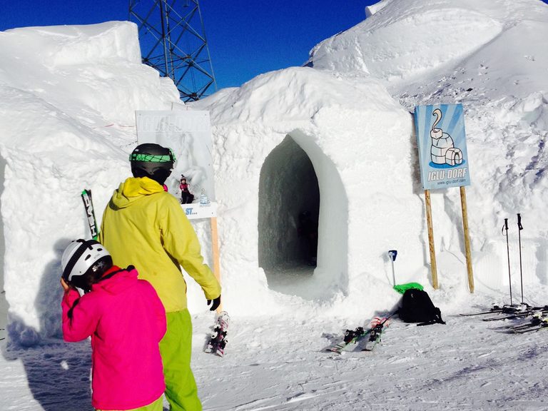 L’ingresso di un igloo, con due ragazzi che lasciano gli sci fuori