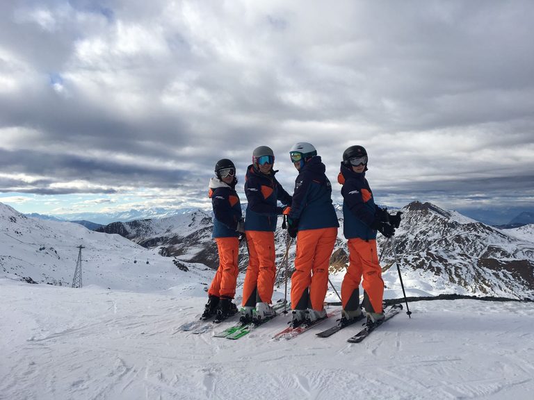 Quattro ragazzi con gli sci ai piedi guardano la valle dalla cima della pista